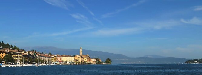 Trip Erlebnisse beliebte Urlaubsziele am Gardasee -  Mit einer Fläche von 370 km² ist der Gardasee der größte See Italiens. Es liegt am Fuße der Alpen und erstreckt sich über drei Staaten: Lombardei, Venetien und Trentino. Die maximale Tiefe des Sees beträgt 346 m, er hat eine längliche Form und sein nördliches Ende ist sehr schmal. Dort ist der See von den Bergen der Gruppo di Baldo umgeben. Du trittst aus deinem gemütlichen Hotelzimmer und es begrüßt dich die warme italienische Sonne. Du blickst auf den atemberaubenden Gardasee, der in zahlreichen Blautönen schimmert - von tiefem Dunkelblau bis zu funkelndem Türkis. Majestätische Berge umgeben dich, während die Brise sanft deine Haut streichelt und der Duft von blühenden Zitronenbäumen deine Nase kitzelt. Du schlenderst die malerischen, engen Gassen entlang, vorbei an farbenfrohen, blumengeschmückten Häusern. Vereinzelt unterbricht das fröhliche Lachen der Einheimischen die friedvolle Stille. Du fühlst dich wie in einem Traum, der nicht enden will. Jeder Schritt führt dich zu neuen Entdeckungen und Abenteuern. Du probierst die köstliche italienische Küche mit ihren frischen Zutaten und verführerischen Aromen. Die Sonne geht langsam unter und taucht den Himmel in ein leuchtendes Orange-rot - ein spektakulärer Anblick.
